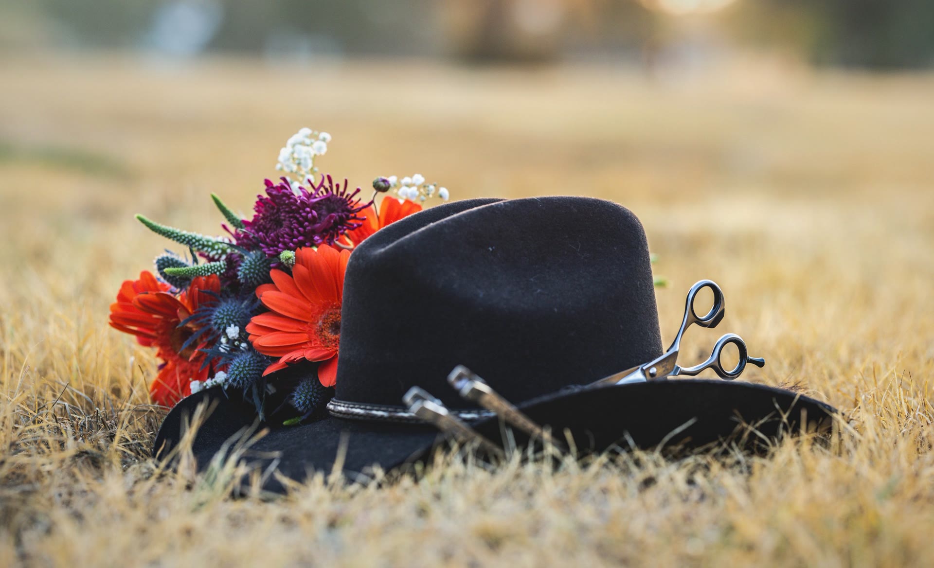 Black cowboy hat with a wildflower bouquet and silver shears resting in dry grass